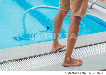 Cleaner of the swimming pool . Man in a blue shirt with cleaning equipment for swimming pools, sunny 61734631