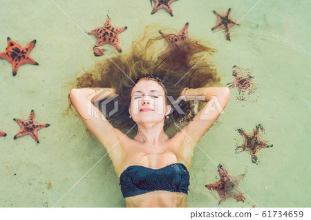 Young woman in the sea with red starfishes Young woman in the sea with red starfishes 61734659