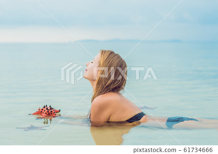 Young woman in the sea with red starfishes Young woman in the sea with red starfishes 61734666