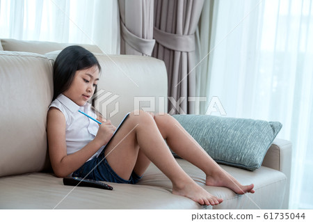 Asian girl doing home work on sofa Asian girl doing home work on sofa 61735044