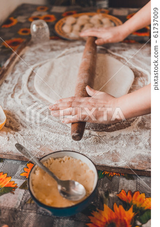 A woman at home rolls out dough for dumplings. A woman at home rolls out dough for dumplings. 61737009