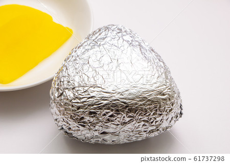 Triangle rice balls wrapped in aluminum foil. In the back of the photo are pickles (takuan pickles) placed on a small plate. Triangle rice balls wrapped in aluminum foil. In the back of the photo are pickles (takuan pickles) placed on a small plate. 61737298