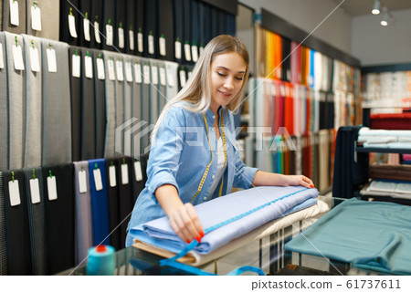 Female seller measures fabric in textile store 61737611