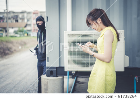 woman walk and chat with friend on smartphone while bandit wear black mask and black clothes holding knife are dodging the corner of the building. woman walk and chat with friend on smartphone while bandit wear black mask and black clothes holding knife are dodging the corner of the building. 61738264