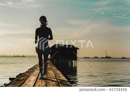 Silhouette of woman jogging in the morning on wooden bridge at sunrise. 61738356