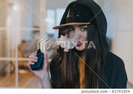 Vaping girl. Young hipster woman vape e-cig at the vapeshop. Hip-hop style. Closeup. Vaping girl. Young hipster woman vape e-cig at the vapeshop. Hip-hop style. Closeup. 61741954