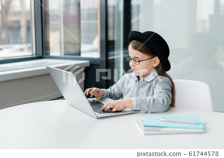 Adorable schoolgirl in casualwear and eyeglasses sitting in front of laptop Adorable schoolgirl in casualwear and eyeglasses sitting in front of laptop 61744578