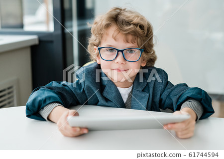 Cute schoolboy with digital tablet looking at you while preparing homework 61744594