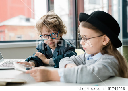 Serious schoolboy in eyeglasses looking at his clever classmate in hat Serious schoolboy in eyeglasses looking at his clever classmate in hat 61744628