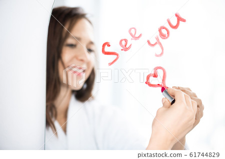 Hand of happy brunette girl writing and drawing heart with lipstick on mirror Hand of happy brunette girl writing and drawing heart with lipstick on mirror 61744829