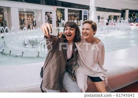 Two girls take a selfie in the mall, a fountain in the background Two girls take a selfie in the mall, a fountain in the background 61745041