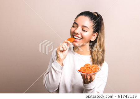 beautiful woman with smile on her face and eyes closed enjoying eating carrot. healthy organic food concept 61745119