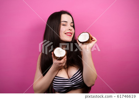 Happy funny girl holds coconut halves near face Happy funny girl holds coconut halves near face 61746619