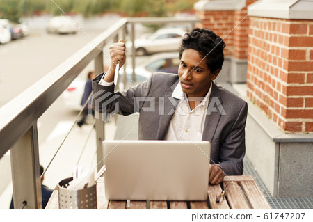 Young handsome Indian man in a summer cafe with a laptop with a table knife Young handsome Indian man in a summer cafe with a laptop with a table knife 61747207