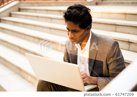 Young handsome Indian man is sitting with a laptop, smiling and typing Young handsome Indian man is sitting with a laptop, smiling and typing 61747209
