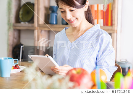 觀看一台片劑計算機的婦女在屋子裡 觀看一台片劑計算機的婦女在屋子裡 61751248