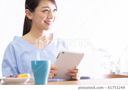 觀看一台片劑計算機的婦女在屋子裡 觀看一台片劑計算機的婦女在屋子裡 61751249