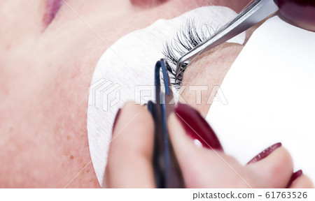 Gluing artificial eyelashes with tweezers. Cosmetic procedure. Eyelash extension. 61763526