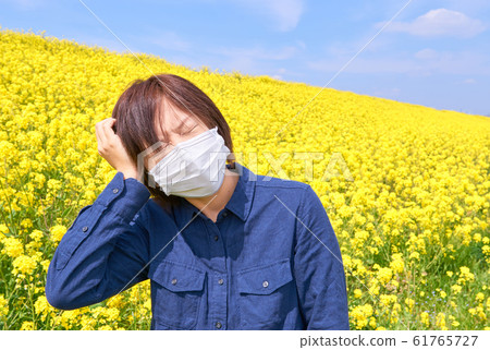 A woman wearing a mask holding her head in a rape field 61765727
