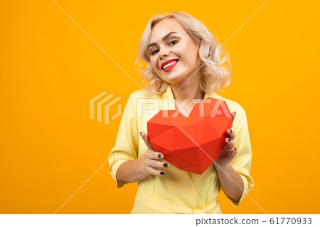 portrait of a blond girl with makeup with a 3-d heart from paper on a yellow background portrait of a blond girl with makeup with a 3-d heart from paper on a yellow background 61770933