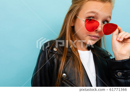 Caucasian teenager girl with brown hair in black jacket holds red sunglasses isolated on blue 61771366