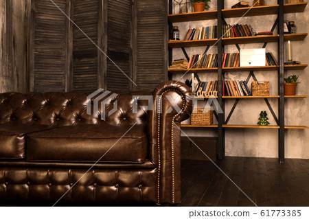 Brown leather sofa in an interior room with a bookcase. Brown leather sofa in an interior room with a bookcase. 61773385