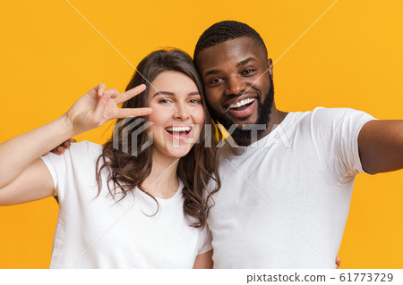 Joyful two international friends taking selfie together and showing peace sign 61773729