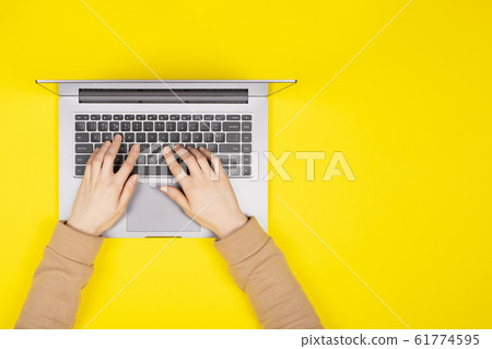 Female hands working on new laptop on bright yellow background Top view, flat lay. Female hands working on new laptop on bright yellow background Top view, flat lay. 61774595