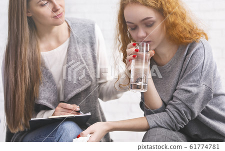 Psychotherapist comforting female patient, giving her glass of water to calm Psychotherapist comforting female patient, giving her glass of water to calm 61774781