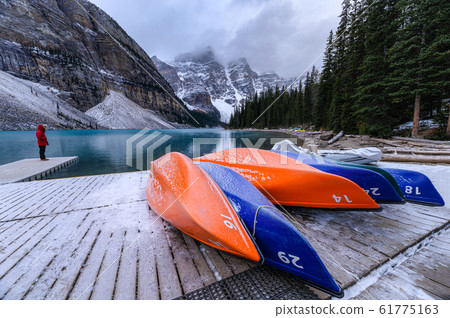 Canoe parked on wooden pier with rocky mountains 61775163
