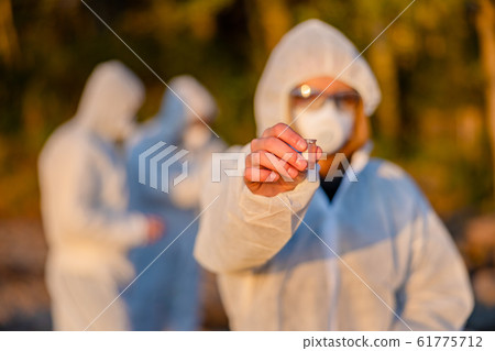 Scientist in white protective suit holding water sample at beach Scientist in white protective suit holding water sample at beach 61775712