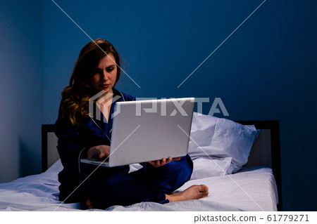 Picture of the woman suffering of insomnia and feeling asleep and working on a laptop at home sitting on the bed. 61779271