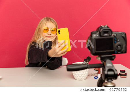 Happy girl at home speaking in front of camera for vlog. Teenage kid working as blogger, recording video tutorial for Internet. Happy girl at home speaking in front of camera for vlog. Teenage kid working as blogger, recording video tutorial for Internet. 61779362