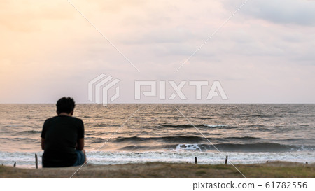 Blur image of a solitary man sitting alone at the beach in sunset time. Blur image of a solitary man sitting alone at the beach in sunset time. 61782556