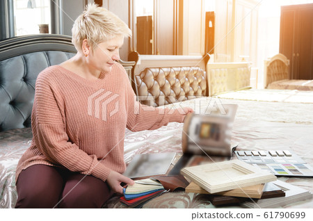 Stylish stylish woman with a short haircut sits on a bed in a furniture store and looks at upholstery probes. She chooses furniture for herself Stylish stylish woman with a short haircut sits on a bed in a furniture store and looks at upholstery probes. She chooses furniture for herself 61790699