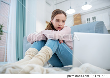 Teen girl sitting on the floor looking at laptop screen. Teen girl sitting on the floor looking at laptop screen. 61791582
