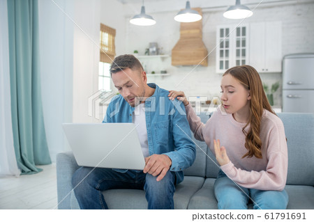Father with laptop and daughter talking on the couch. 61791691