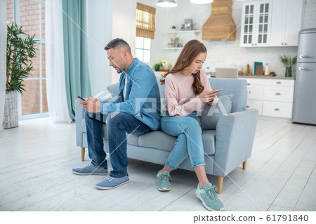 Father and daughter turning away from each other sitting on couch. 61791840