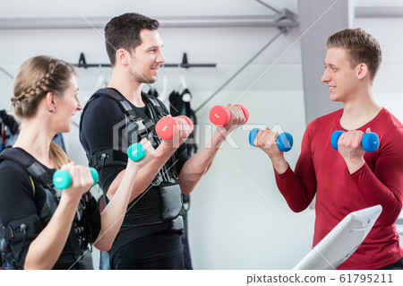 Personal trainer working with couple in ems center to train the biceps Personal trainer working with couple in ems center to train the biceps 61795211
