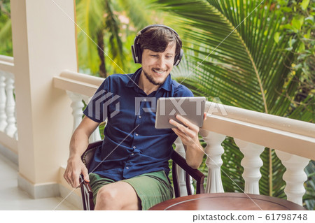 man in tropics talking with friends and family on video call using a tablet and wireless headphones man in tropics talking with friends and family on video call using a tablet and wireless headphones 61798748