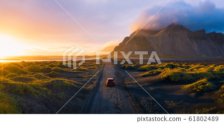 Gravel road at sunset with Vestrahorn mountain and a car driving, Iceland 61802489