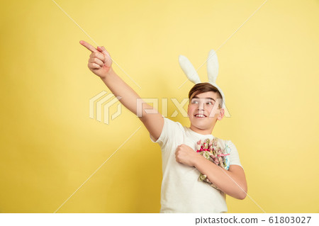 Easter bunny boy with bright emotions on yellow studio background 61803027