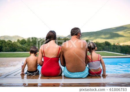 Rear view of family with two small children by swimming pool outdoors. 61806783
