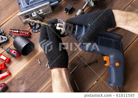 the master repairs a broken electrical device: drill, cutter on a wooden table. Electric Tool Repair Shop 61811585
