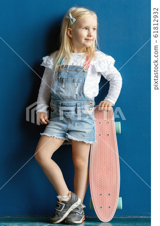 Happy 3 years old toddler girl holding pink plastic skateboard while standing against blue wall 61812932