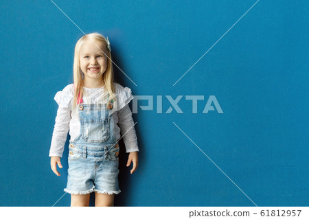 Happy 3-year-old toddler girl smiling while posing against blue wall 61812957