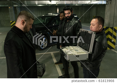 Mature man in black jacket, gloves and jeans opening suitcase with dollars 61813908