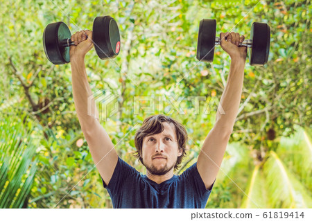 Bicep curl - weight training fitness man outside working out arms lifting dumbbells doing biceps curls. Male sports model exercising outdoors as part of healthy lifestyle Bicep curl - weight training fitness man outside working out arms lifting dumbbells doing biceps curls. Male sports model exercising outdoors as part of healthy lifestyle 61819414