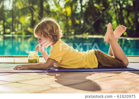 Boy drinking green smoothie lying by the pool 61820975
