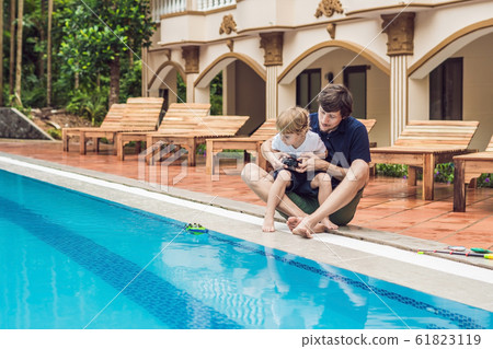 Father and son playing with a remote controlled boat in the pool 61823119